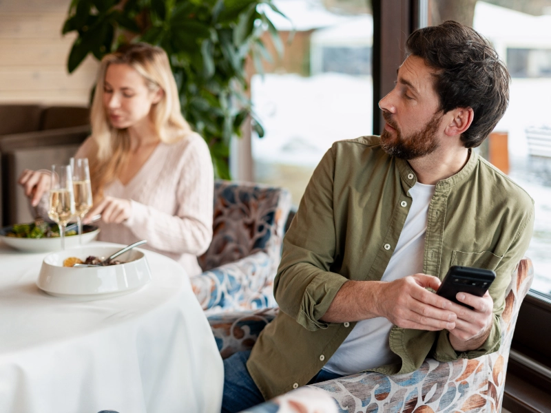 A man at a restaurant table looks away from his date while holding his phone